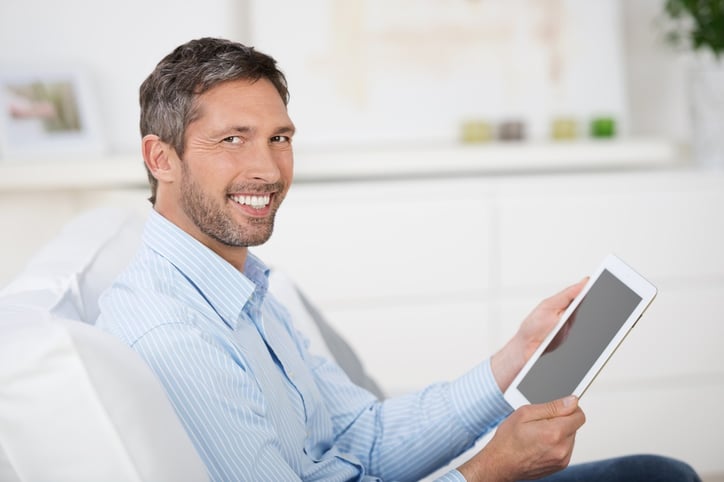 Side view of mature man reading ebook at digital tablet while sitting on sofa at home.jpeg